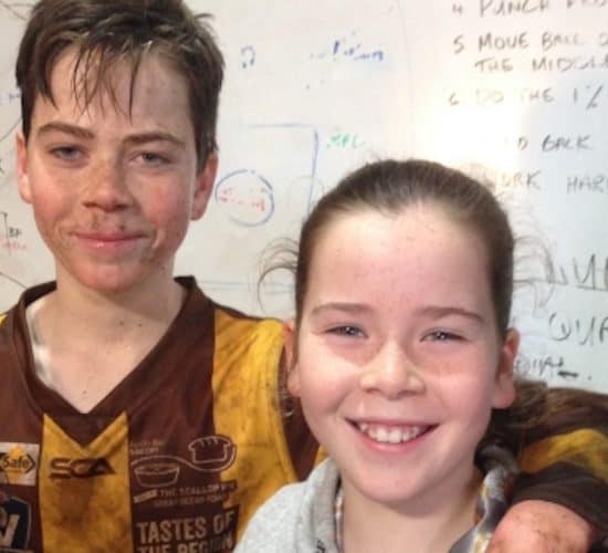 Two children in sports attire, one wearing a muddy jersey, the other smiling, stand in front of a whiteboard with handwritten notes highlighting their efforts for a charity event. Two children in sports attire, one wearing a muddy jersey, the other smiling, stand in front of a whiteboard with handwritten notes highlighting their efforts for a charity event.