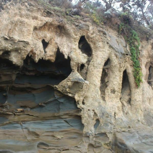 A rocky cliff face with irregular, eroded formations and sparse vegetation on the upper areas.