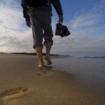 Seaside walk along sandy beach with footprints and ocean view at sunset.