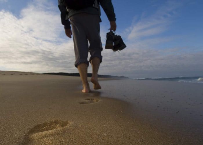 Seaside walk along sandy beach with footprints and ocean view at sunset.