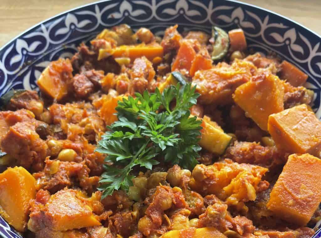 A close-up of a vegetable stew with chunks of sweet potato, chickpeas, and herbs, garnished with fresh parsley in a patterned bowl—perfect nourishment after completing the Great Ocean Walk.