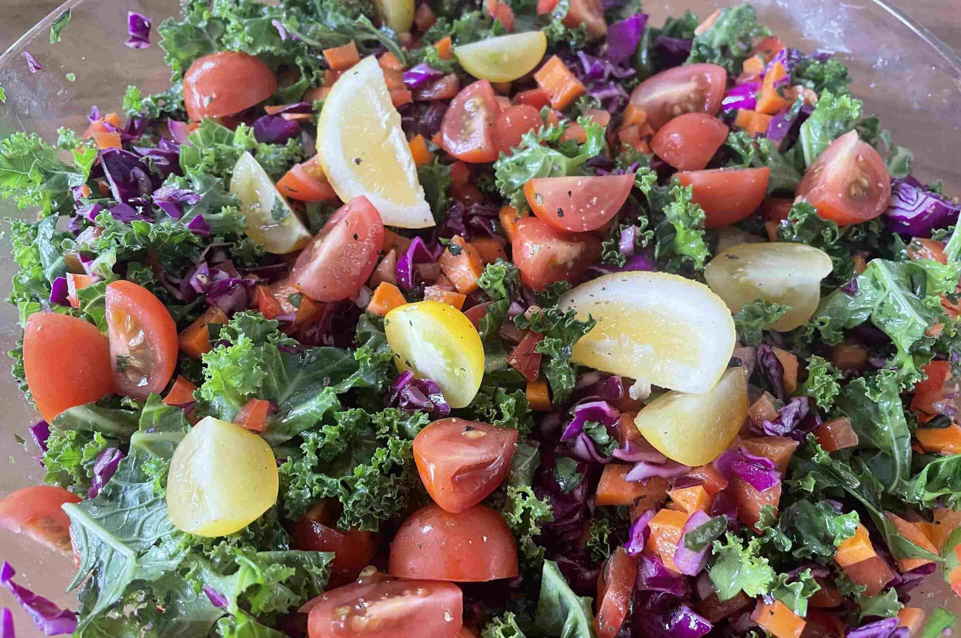 A bowl of fresh salad with kale, cherry tomatoes, red cabbage, carrots, and lemon wedges—perfect for those seeking sustainable food on the Great Ocean Walk.