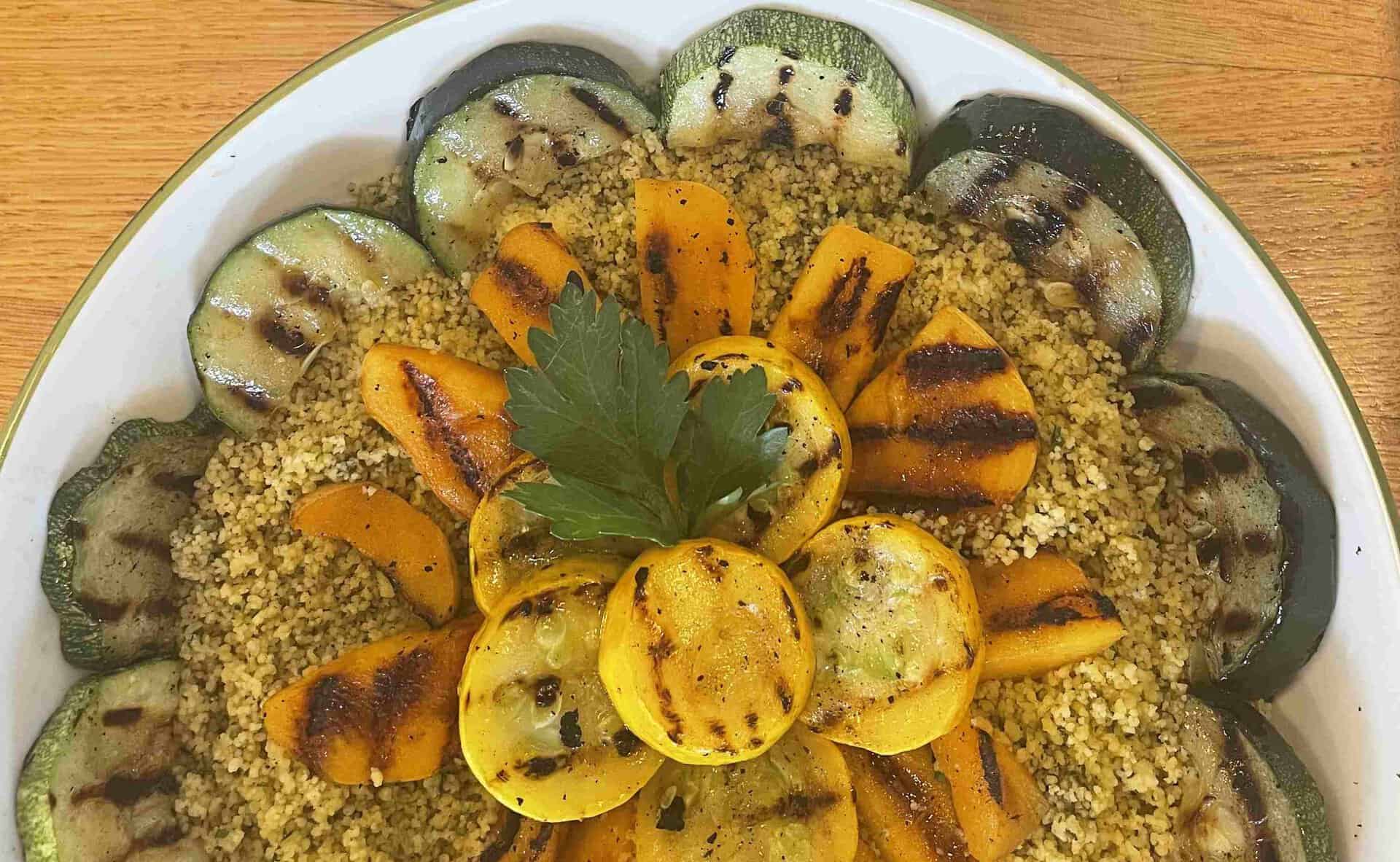 A plate of couscous topped with grilled yellow courgette and courgette slices, garnished with fresh parsley.